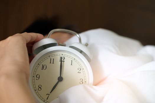 A close-up of a hand reaching for a ringing alarm clock, symbolizing waking up in the morning.